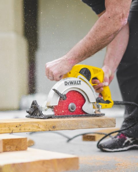 man in black sweatpants using DEWALT circular saw and cutting a wood plank