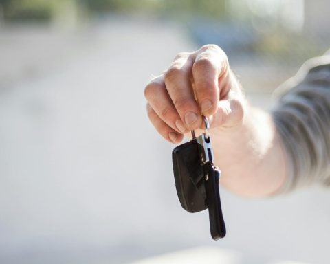 Close-up of a hand handing over car keys, signifying purchase or rental.