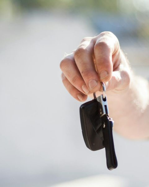 Close-up of a hand handing over car keys, signifying purchase or rental.