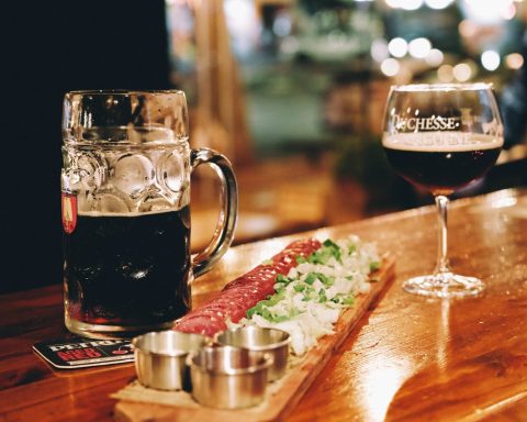 A wooden table topped with a glass of beer and a plate of food