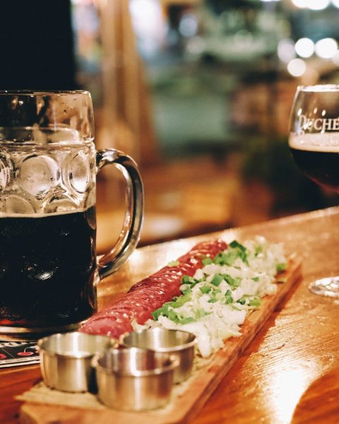 A wooden table topped with a glass of beer and a plate of food