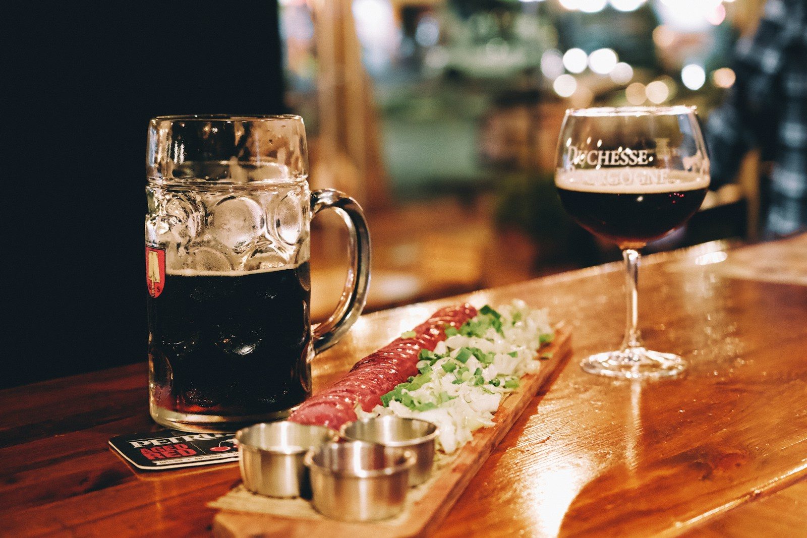 A wooden table topped with a glass of beer and a plate of food