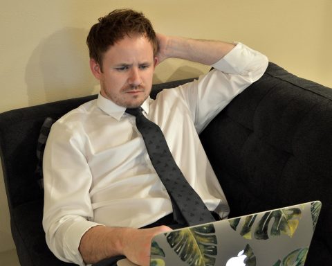 Jonge man werkt op laptop thuis naast zijn vaste baan
